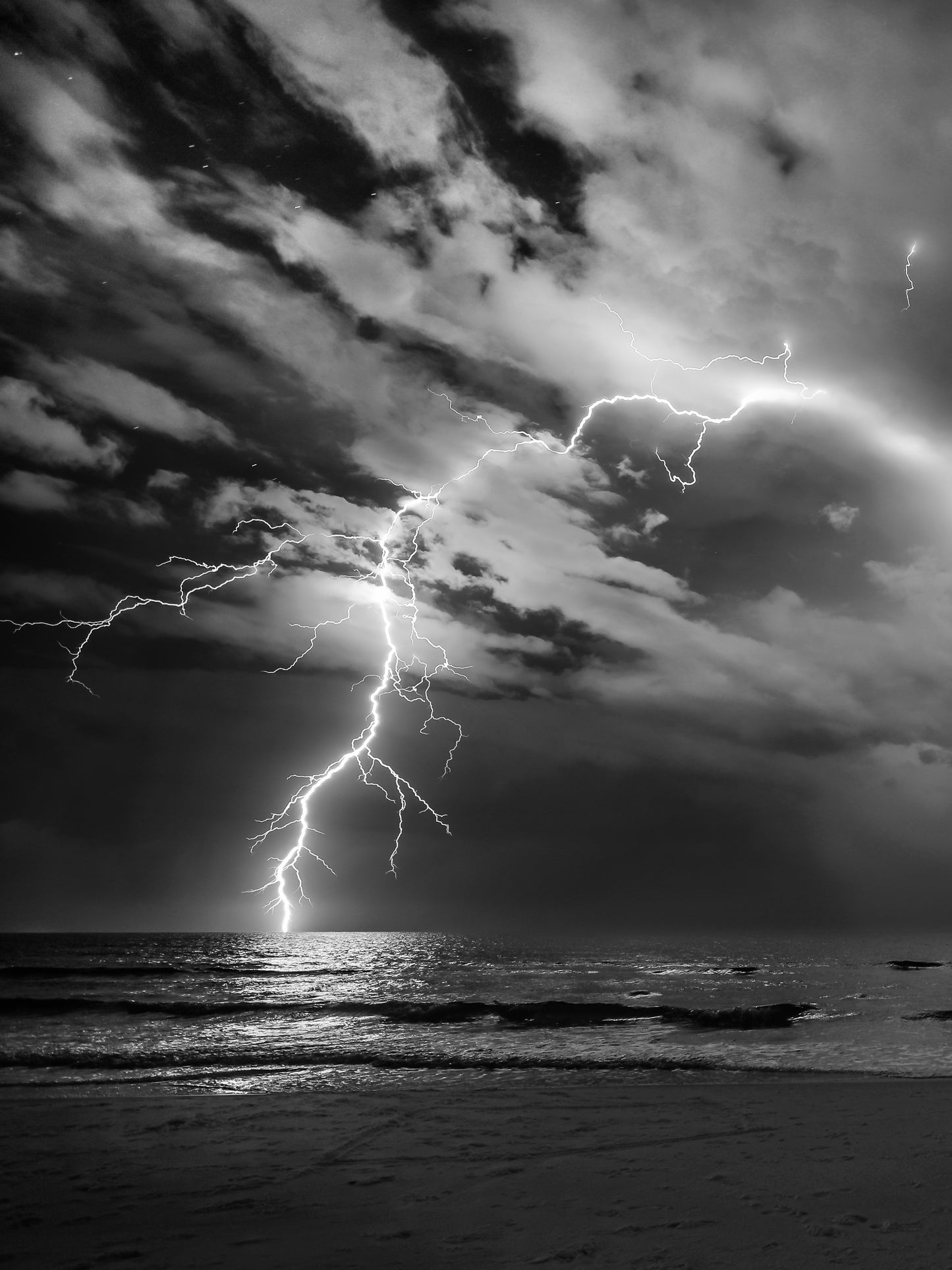 A black-and-white lightning bolt strikes the Gulf over an empty beach — fine art storm photography by Susan Gunn.