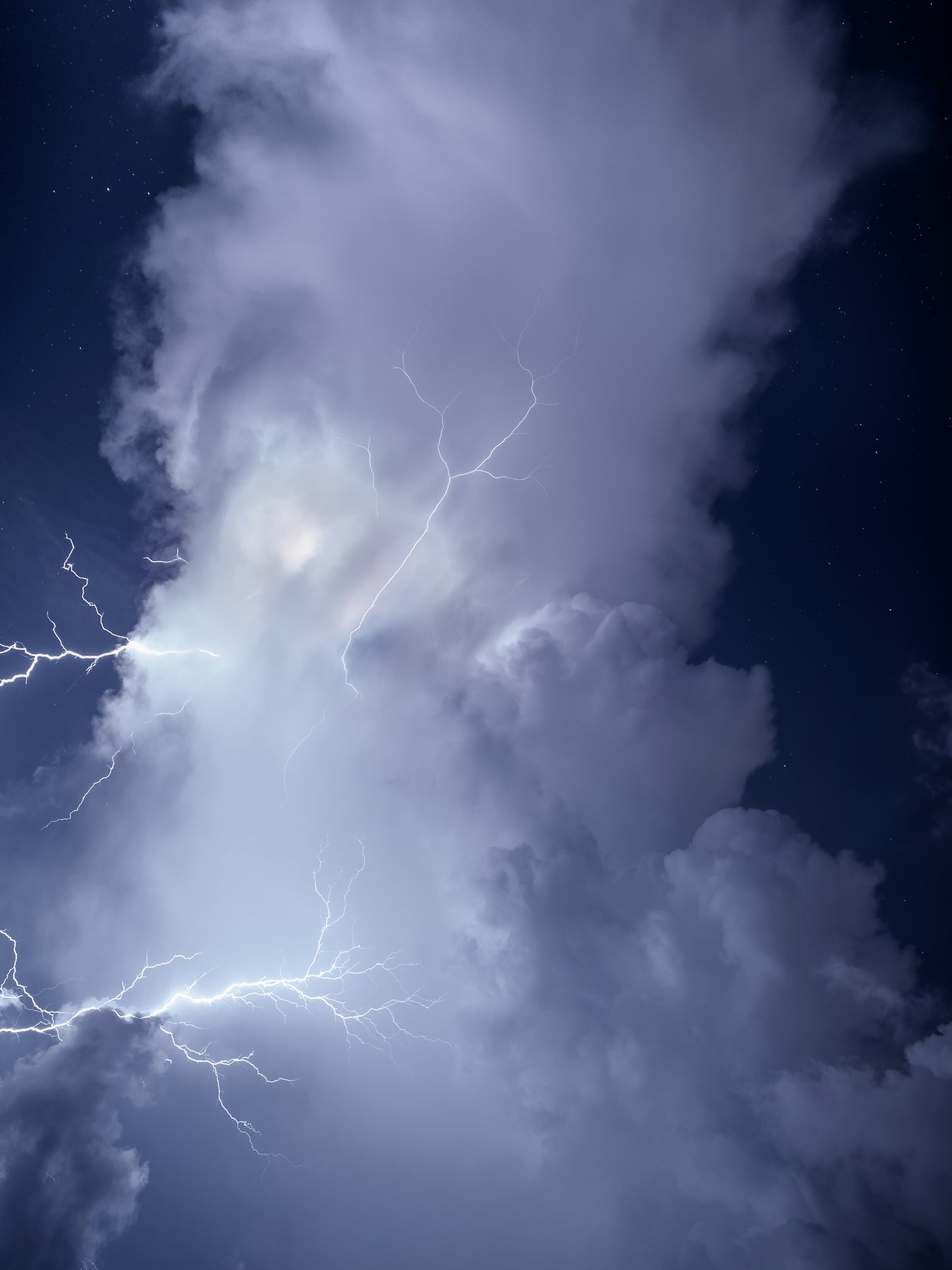 A towering storm cloud glowing against a deep blue starry night sky with spider lightning crawling through it — fine art storm photography by Susan Gunn.
