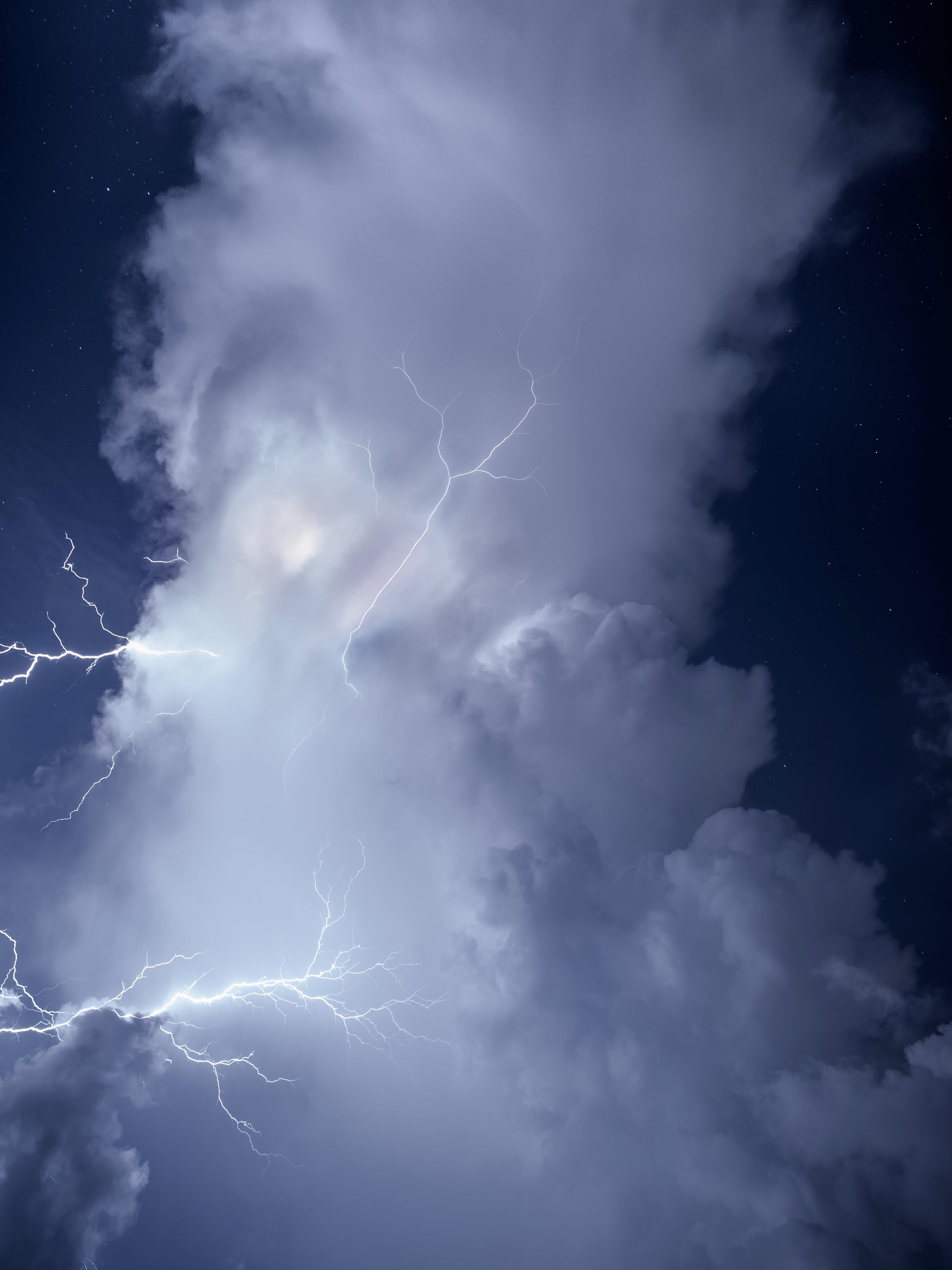 A towering storm cloud glowing against a deep blue starry night sky with spider lightning crawling through it — fine art storm photography by Susan Gunn.